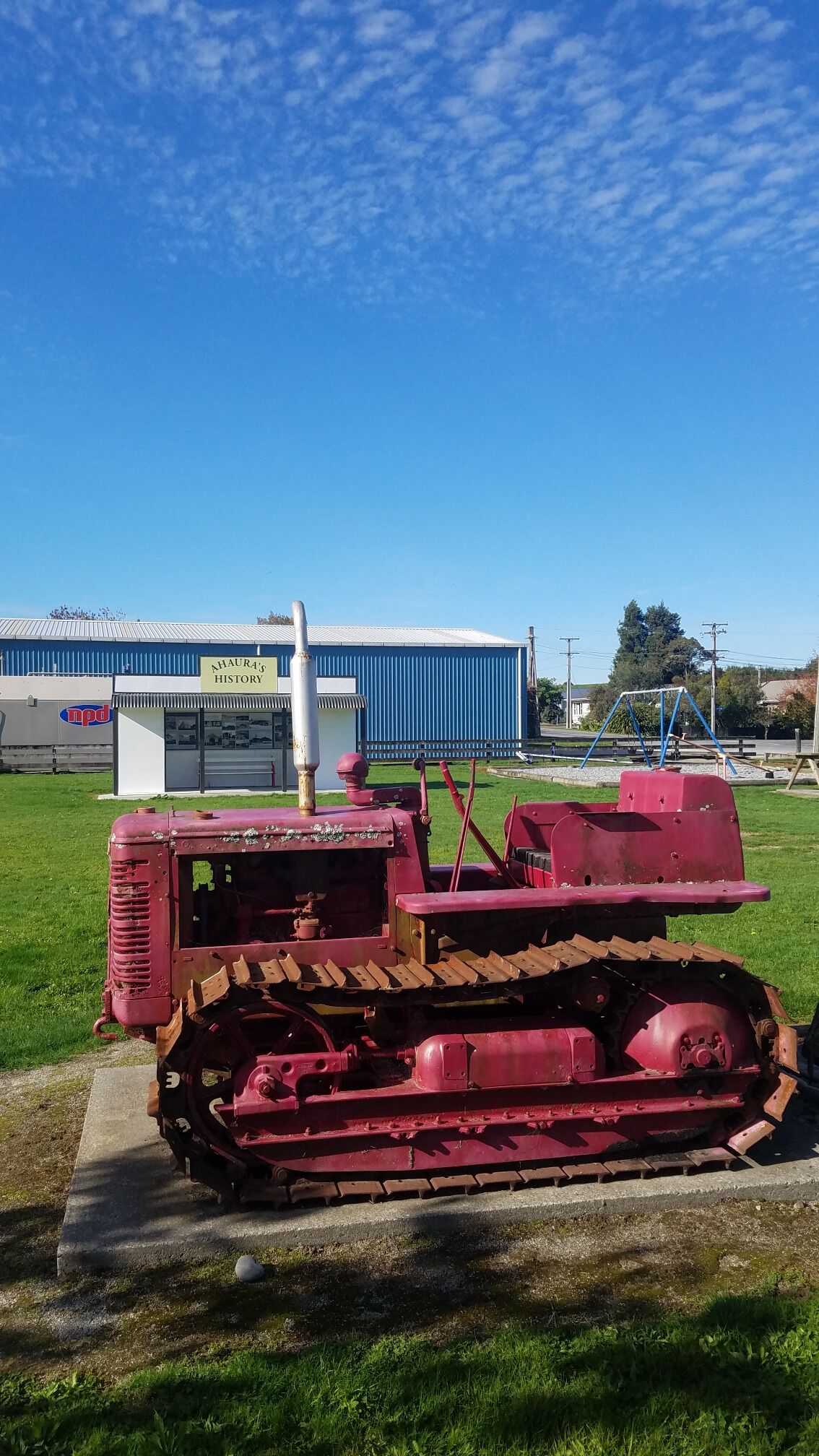 A red tractor on a grassy field with a blue building in the background.