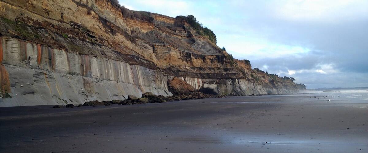 A coastal cliff with layered sedimentary rock formations and a sandy beach.