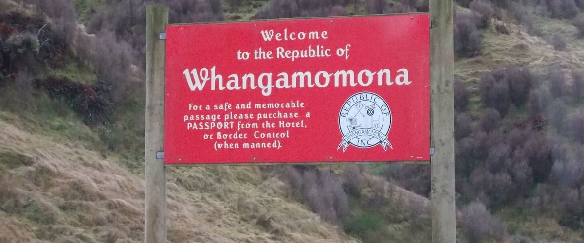 A red welcome sign for the Republic of Whangamomona, advising visitors to purchase a passport from the Hotel or Border Control.