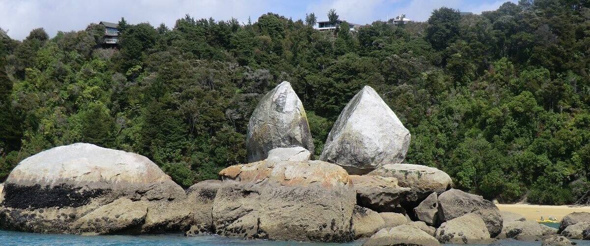A coastal landscape with large boulders and a forested hill in the background.