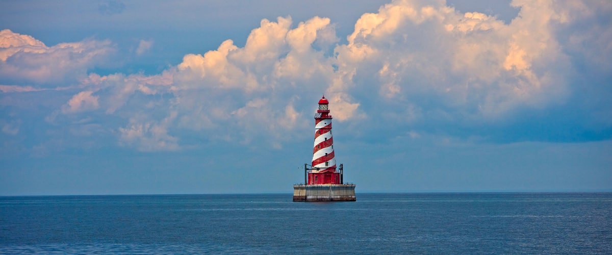 A red and white striped lighthouse on a small island in the ocean.