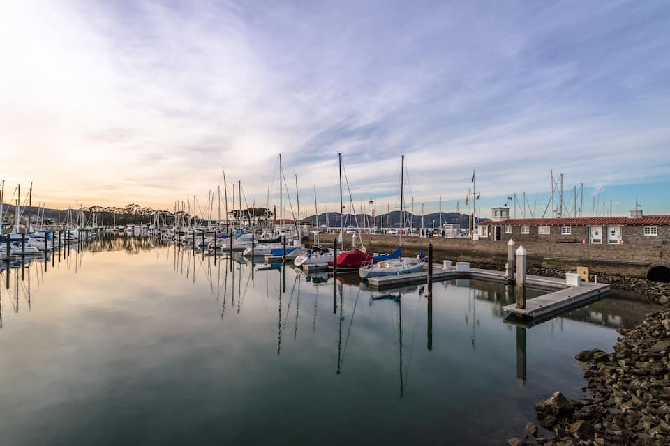 A marina with boats docked, calm water, and a clear sky.