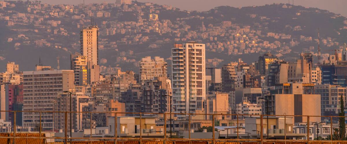 A cityscape with a prominent tall building in the foreground, a dense cluster of buildings in the background, and a hilly terrain.