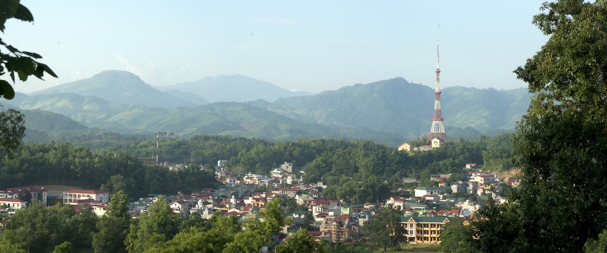 A town with a prominent tower, surrounded by lush green hills and dense forests.