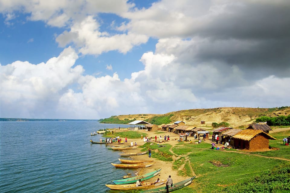 A lakeside village with traditional huts and canoes by the water.