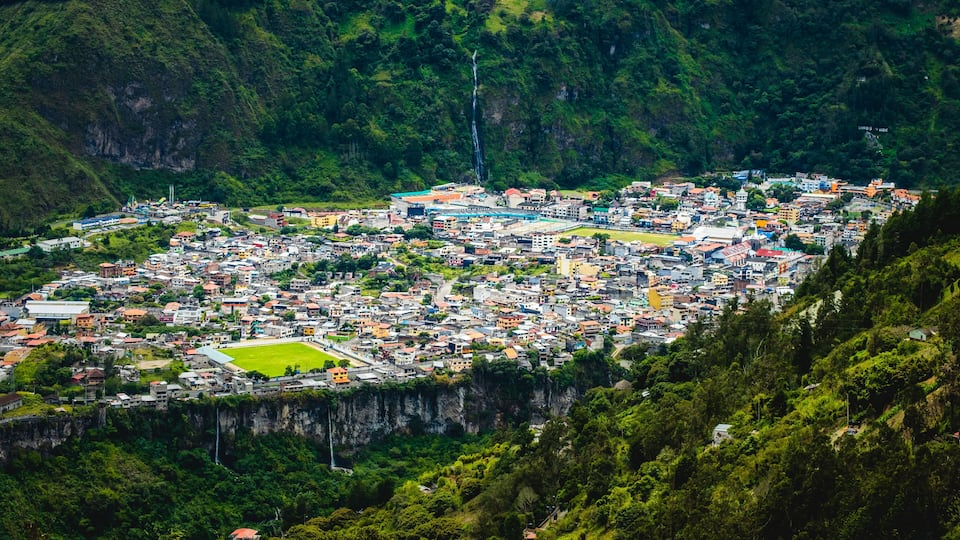 A town nestled in a valley with a waterfall and lush greenery.