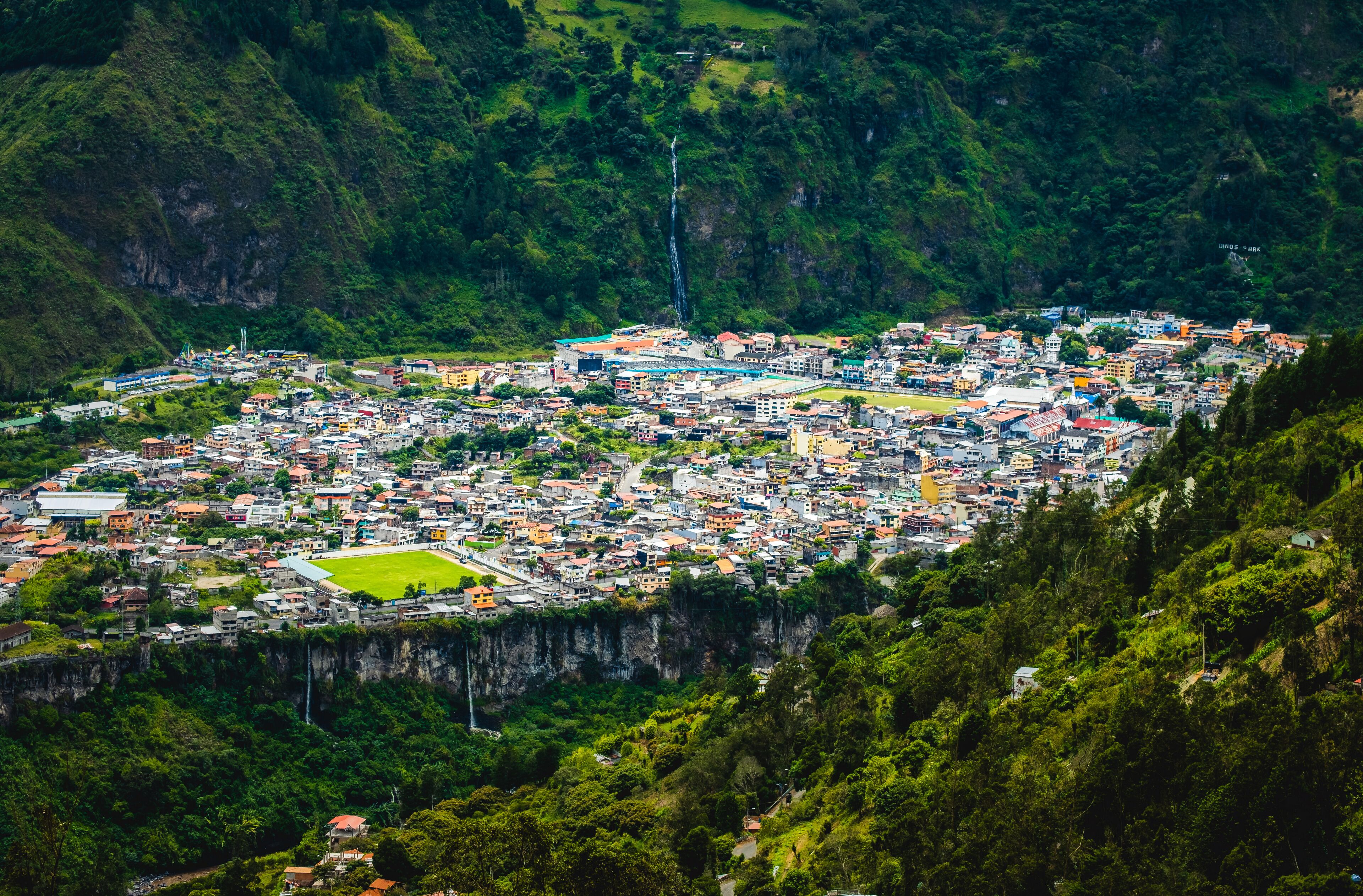 A town nestled in a valley with a waterfall and lush greenery.