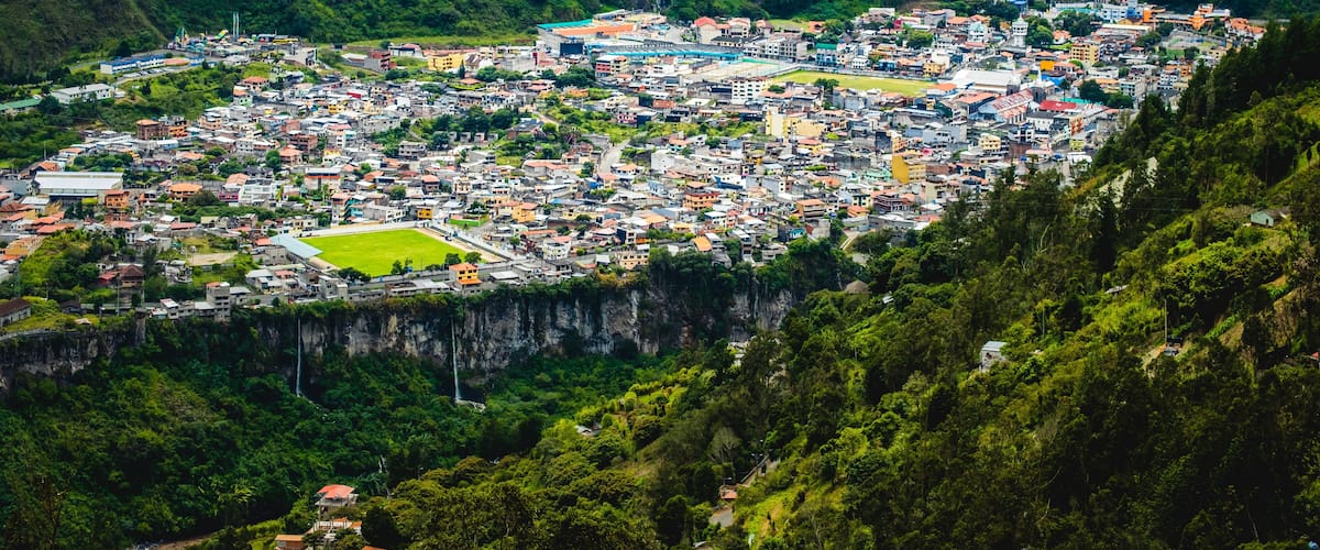A town nestled in a valley with a waterfall and lush greenery.