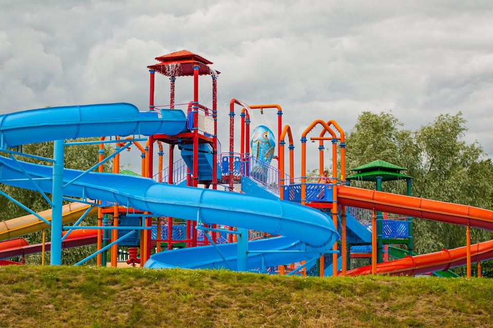 Un parco acquatico colorato con scivoli blu e arancioni e un'area giochi verde.
