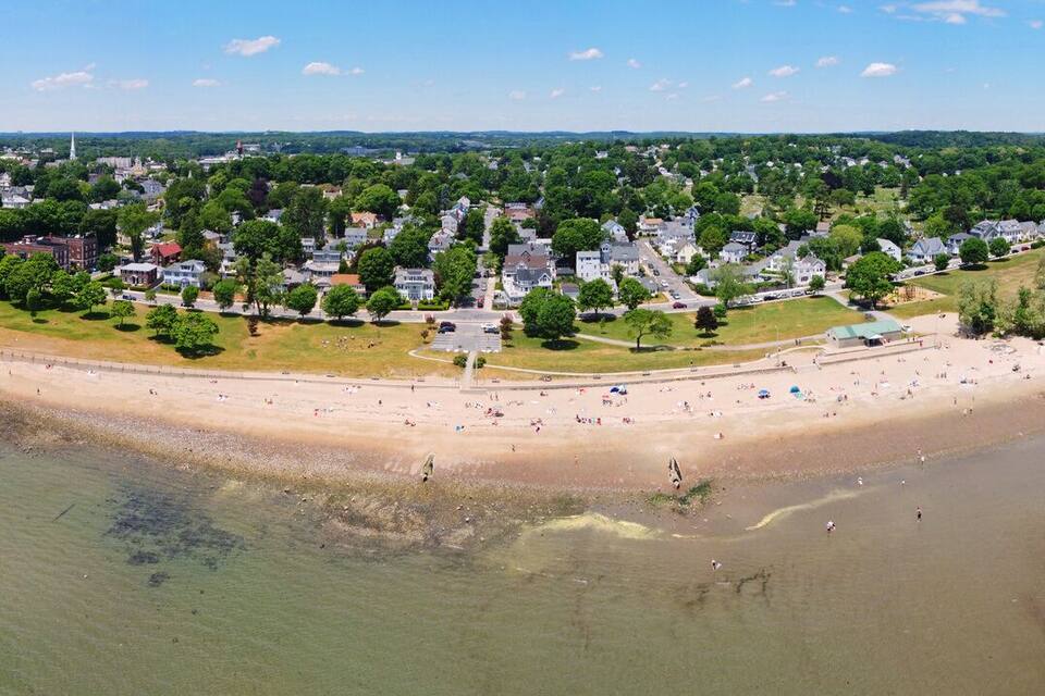 An aerial view of a coastal town with a beach, houses, and a bay.