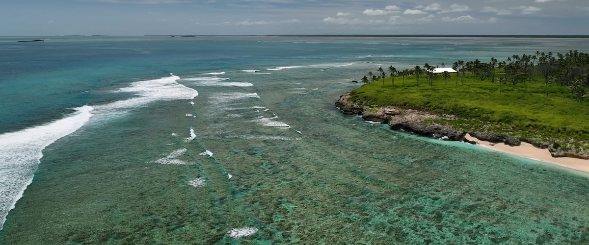 A tropical island with clear turquoise waters, a sandy beach, and a small cluster of palm trees.