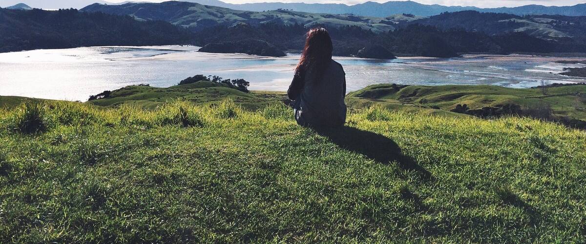 A person sitting on a grassy hill overlooking a lake and mountains.