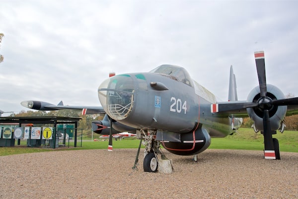 Un avion militaire portant le numéro 204 sur le devant de la carlingue, stationné sur une surface de gravier, avec un champ herbeux et des arbres en arrière-plan.