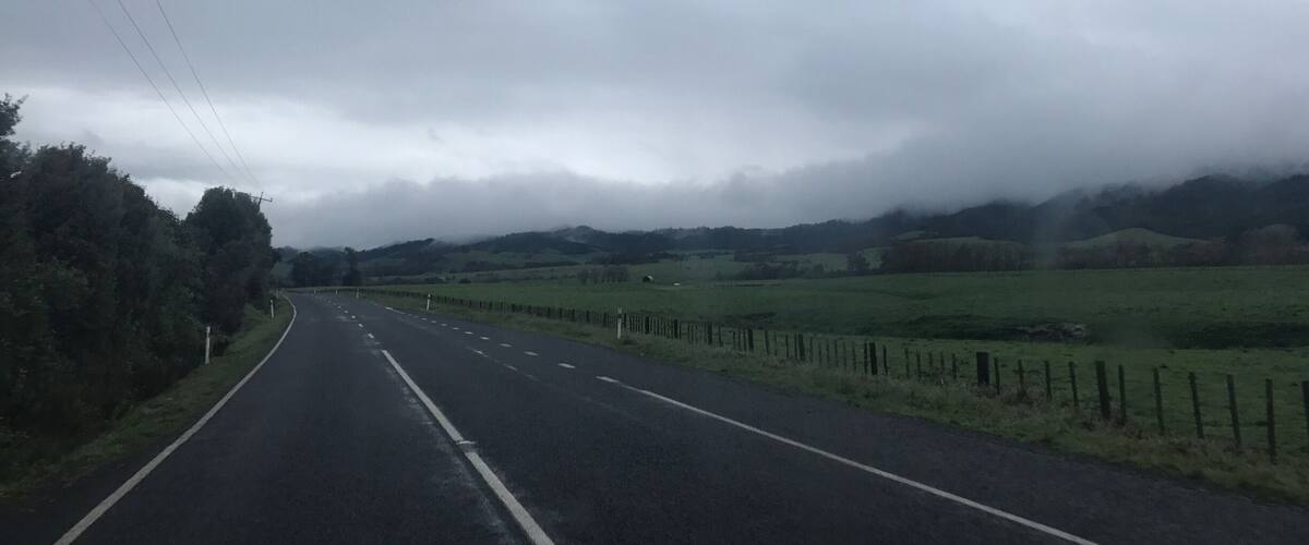 A rural road curving through a hilly landscape with a cloudy sky.