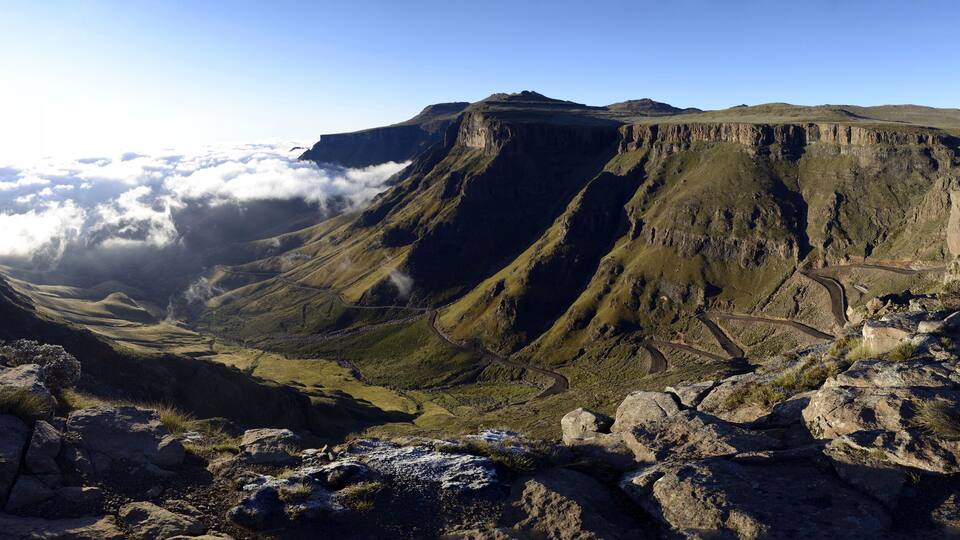 A mountainous landscape with a winding road, rocky terrain, and a valley below.