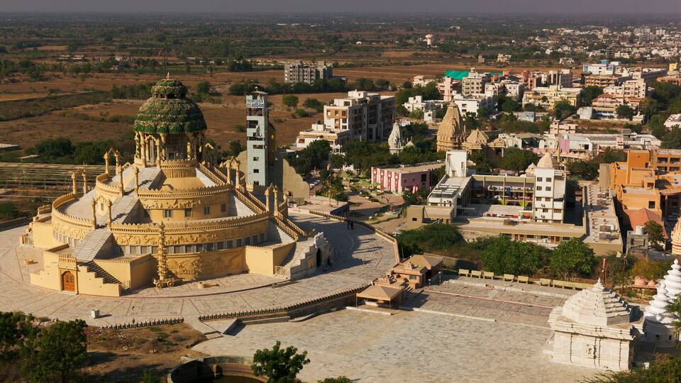 A historic temple complex with intricate architecture, surrounded by a mix of modern and traditional buildings in a semi-urban setting.