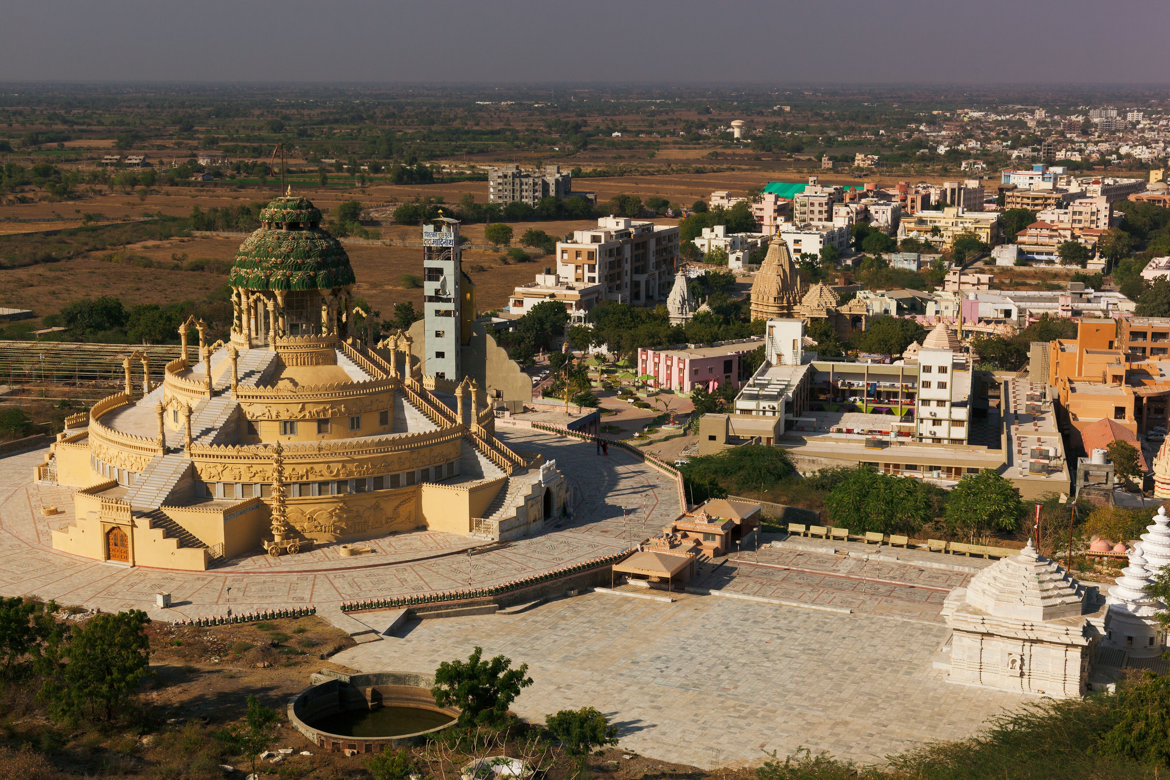 A historic temple complex with intricate architecture, surrounded by a mix of modern and traditional buildings in a semi-urban setting.