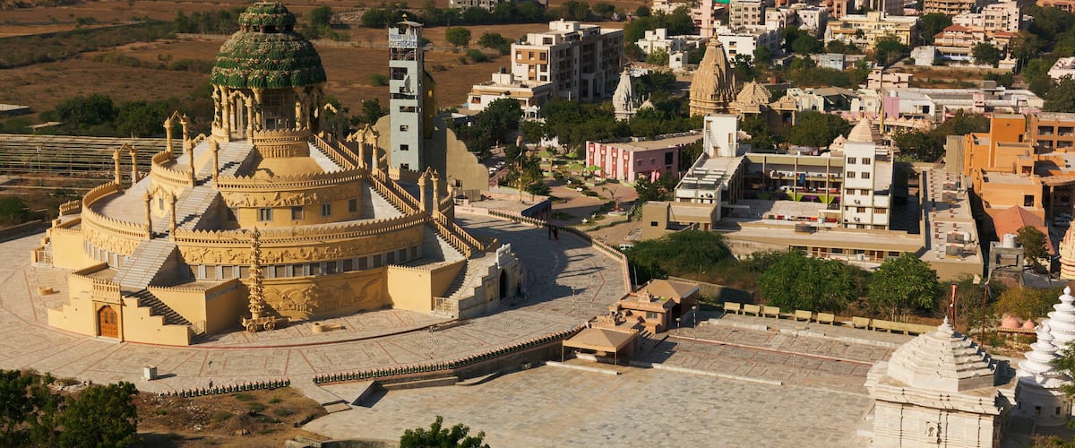 A historic temple complex with intricate architecture, surrounded by a mix of modern and traditional buildings in a semi-urban setting.