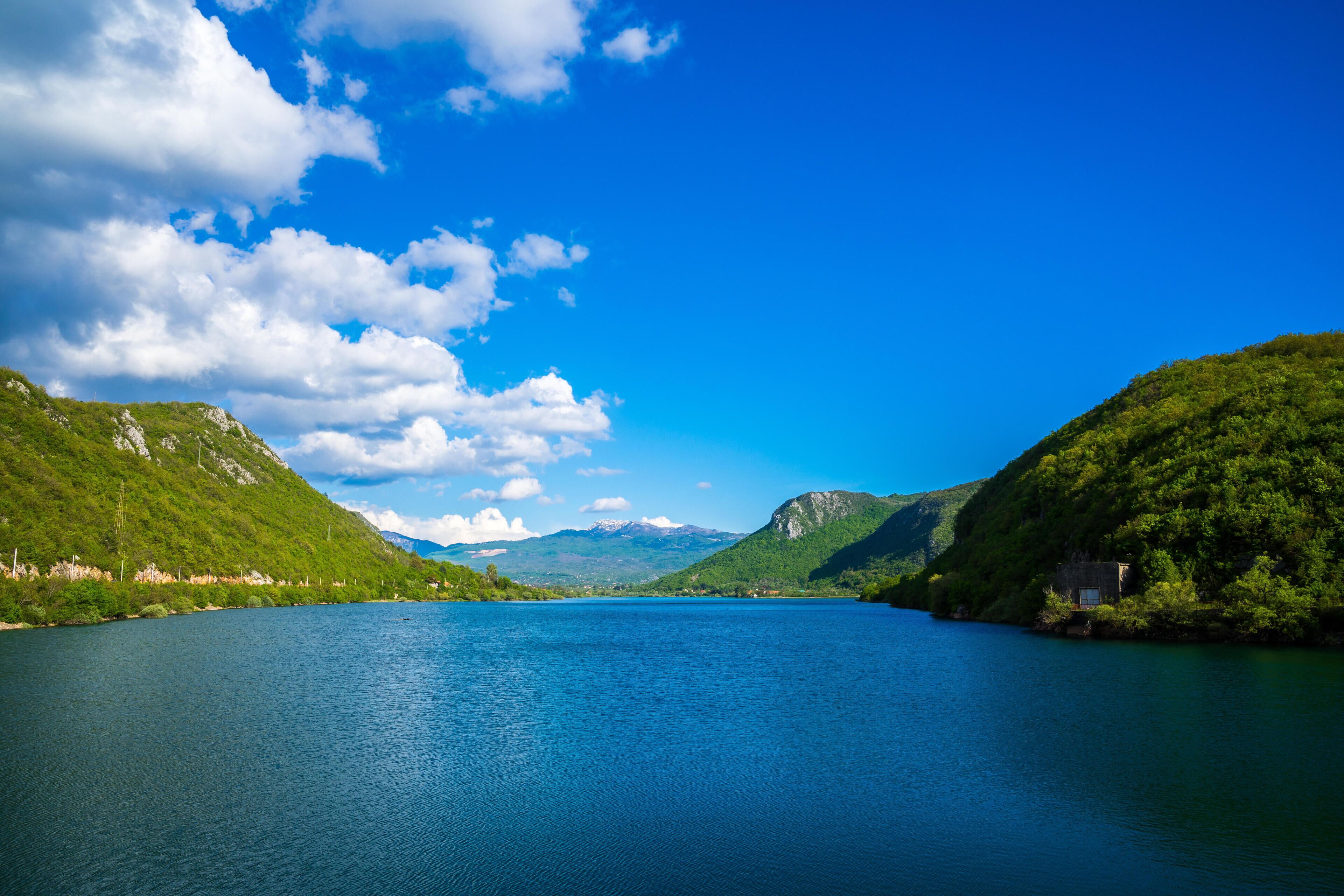 A calm lake surrounded by lush green hills and mountains under a clear blue sky.