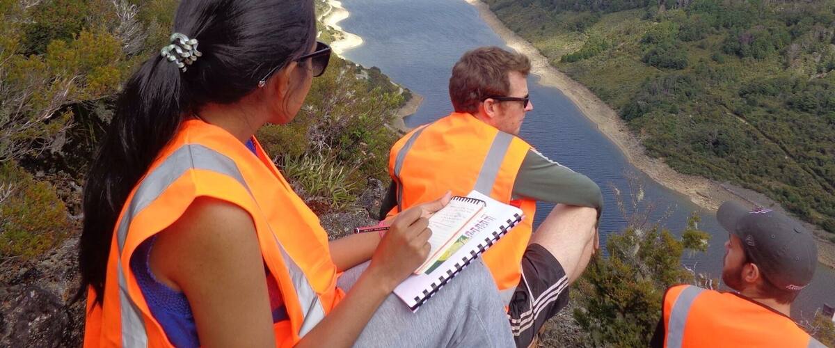 A group of people in orange vests overlooking a river valley with a winding river and hills.