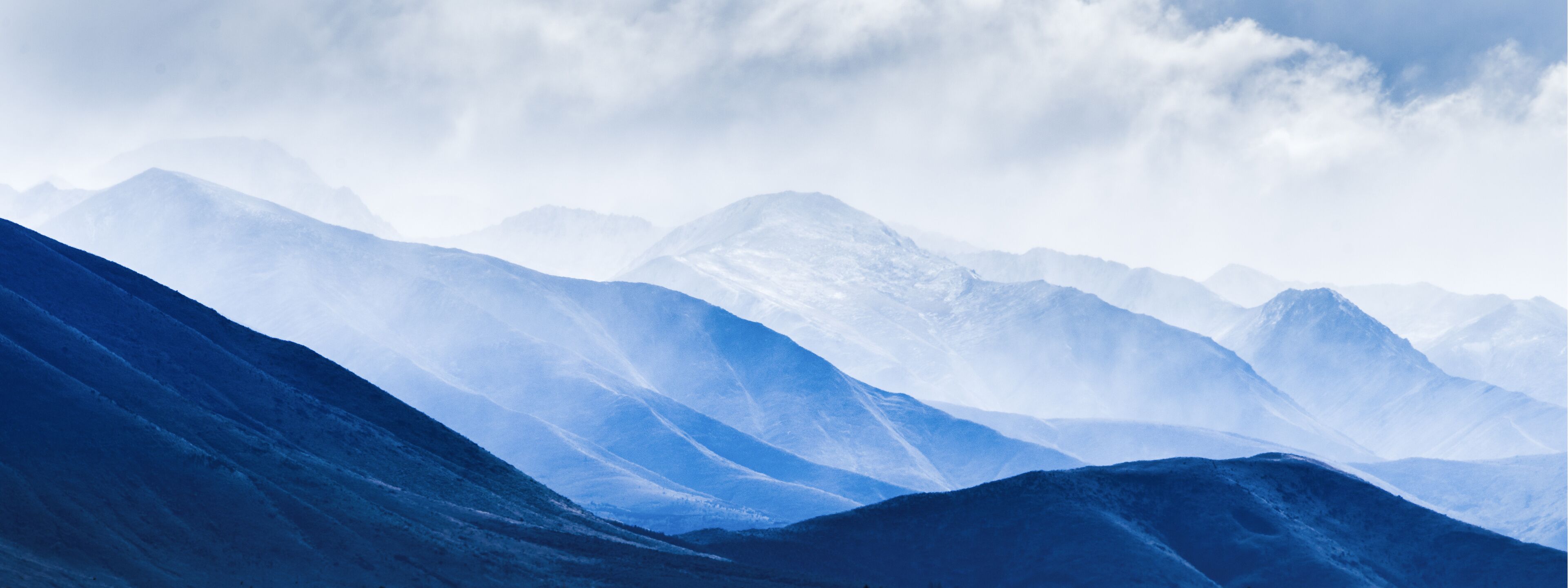 A range of snow-covered mountains under a cloudy sky.