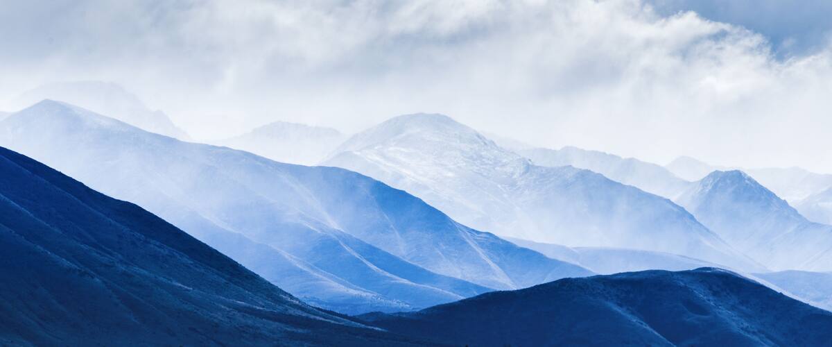 A range of snow-covered mountains under a cloudy sky.