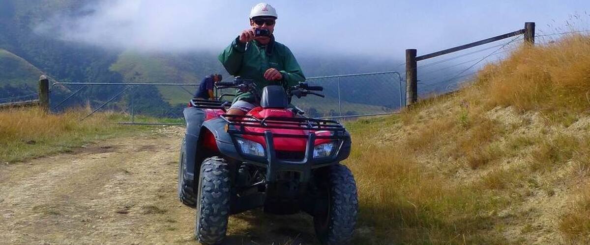 A person on a red ATV on a dirt path with mountains and fog in the background.