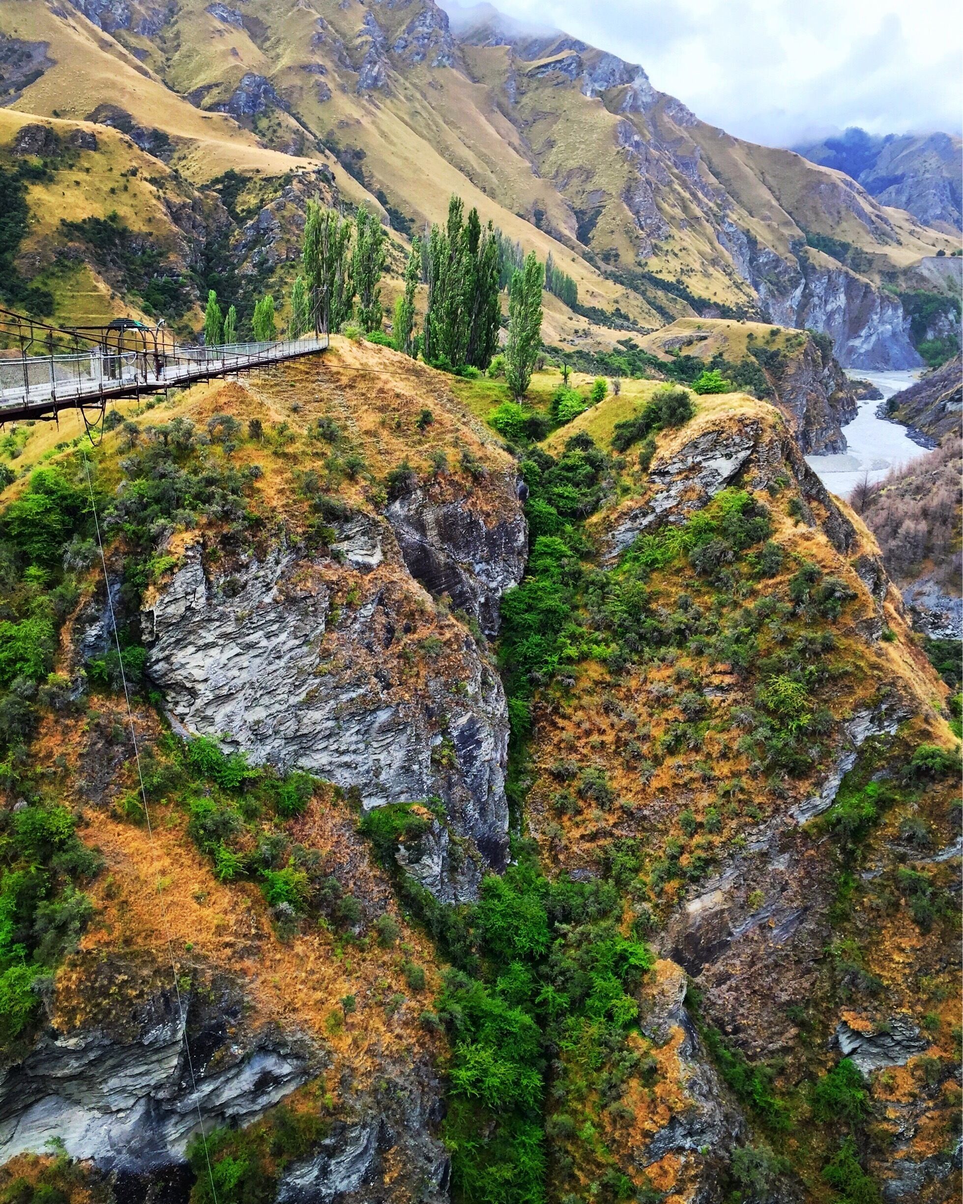 A suspension bridge over a canyon with rocky cliffs and sparse vegetation.
