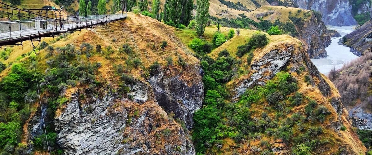 A suspension bridge over a canyon with rocky cliffs and sparse vegetation.