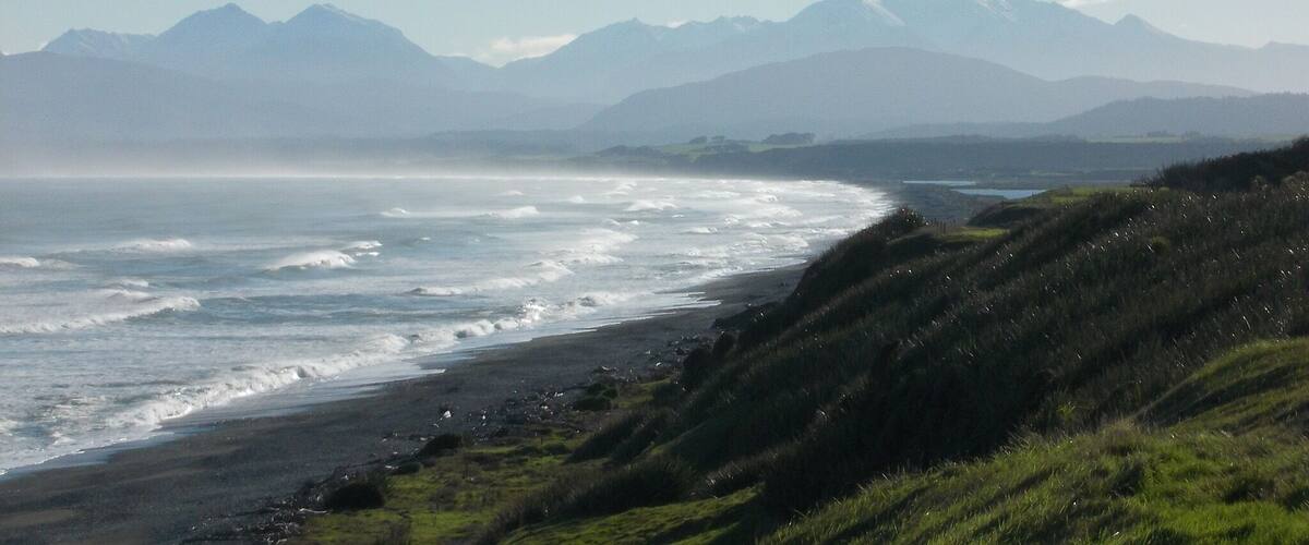 A coastal landscape with a beach, waves, and distant mountains.