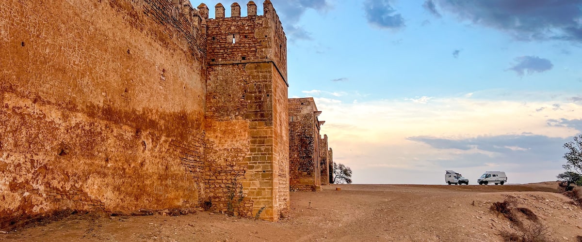 A view of the walls and towers of the Boulaouane Kasbah in the evening light. 2 expedition 4x4s have set up camp at the foot of the fortress