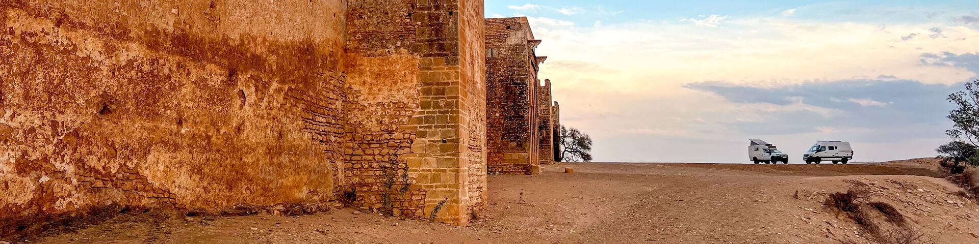 A view of the walls and towers of the Boulaouane Kasbah in the evening light. 2 expedition 4x4s have set up camp at the foot of the fortress