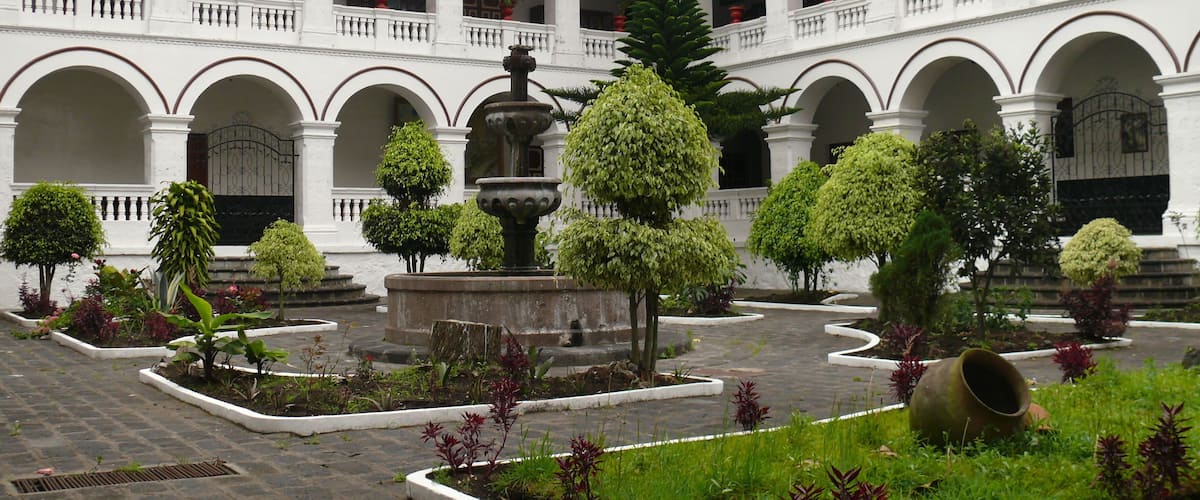 A courtyard with a fountain, potted plants, and a tiled floor.