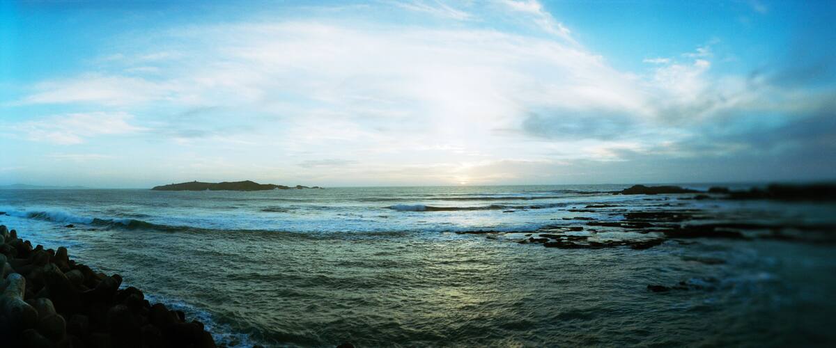 A coastal landscape with waves crashing against rocks and a distant island under a cloudy sky.