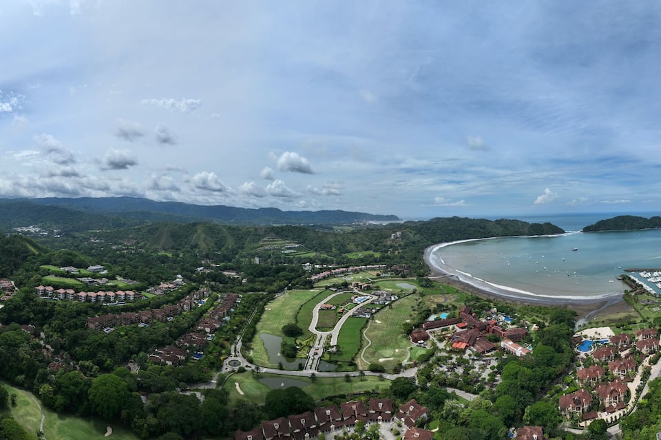 Un resort costero con exuberante vegetación, un campo de golf y una playa.