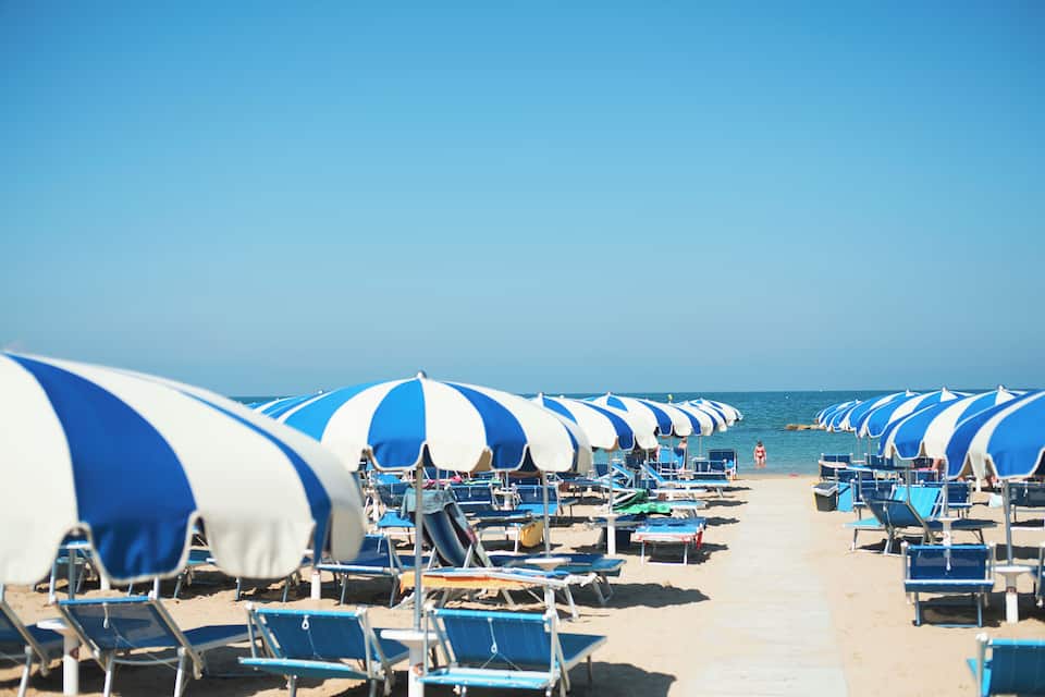 Une plage bordée de rangées de parasols et de chaises longues aux rayures bleues et blanches.