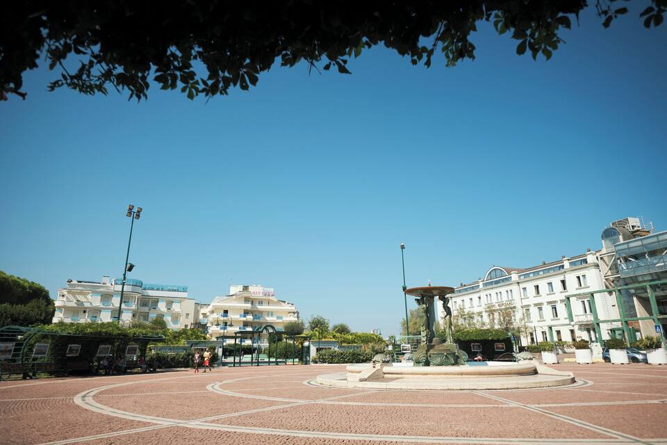 Une place publique avec une fontaine, entourée d’immeubles et d’arbres.