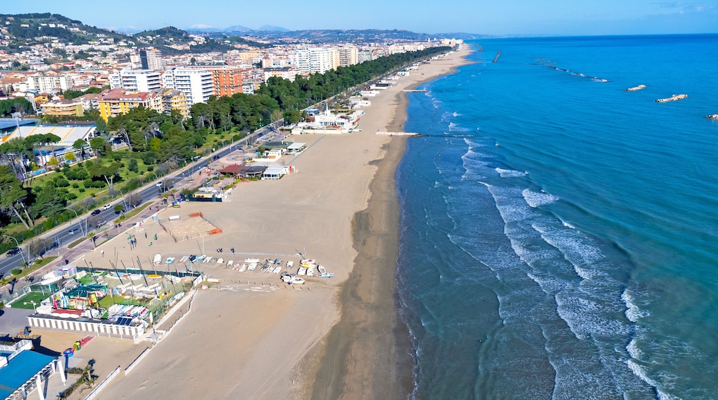 Un paisaje urbano costero con una extensa playa de arena, un mar azul cristalino y una zona urbana densa con edificios y zonas verdes.