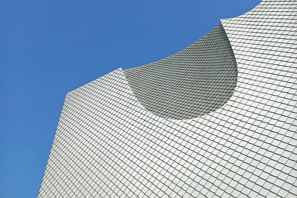 Une structure architecturale moderne, caractérisée par un motif géométrique distinctif et une grande ouverture incurvée qui se détache sur un ciel bleu clair.