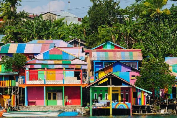 Des maisons colorées, construites sur pilotis, au bord d’une rivière.