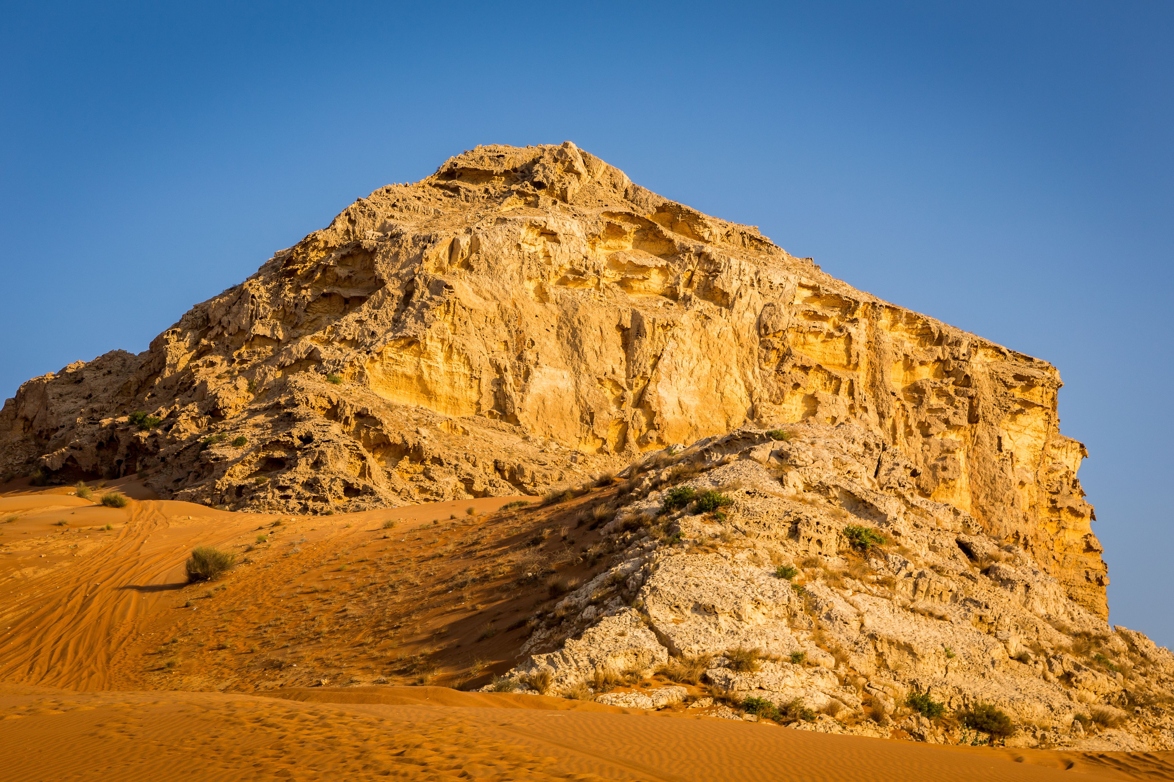 Fossil Rock limestone rock formation in the desert, with sand dunes around, Sharjah, United Arab Emirates.