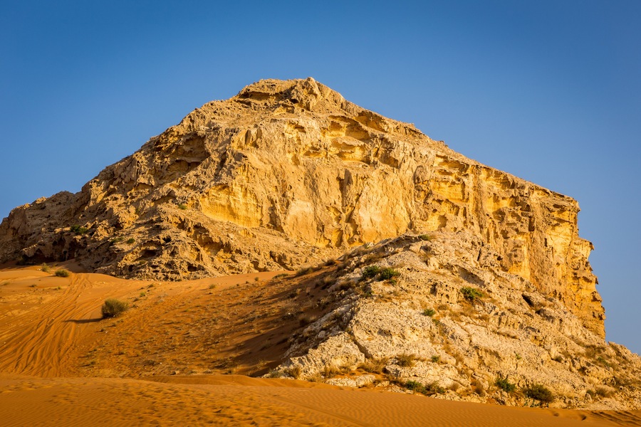 Fossil Rock limestone rock formation in the desert, with sand dunes around, Sharjah, United Arab Emirates.