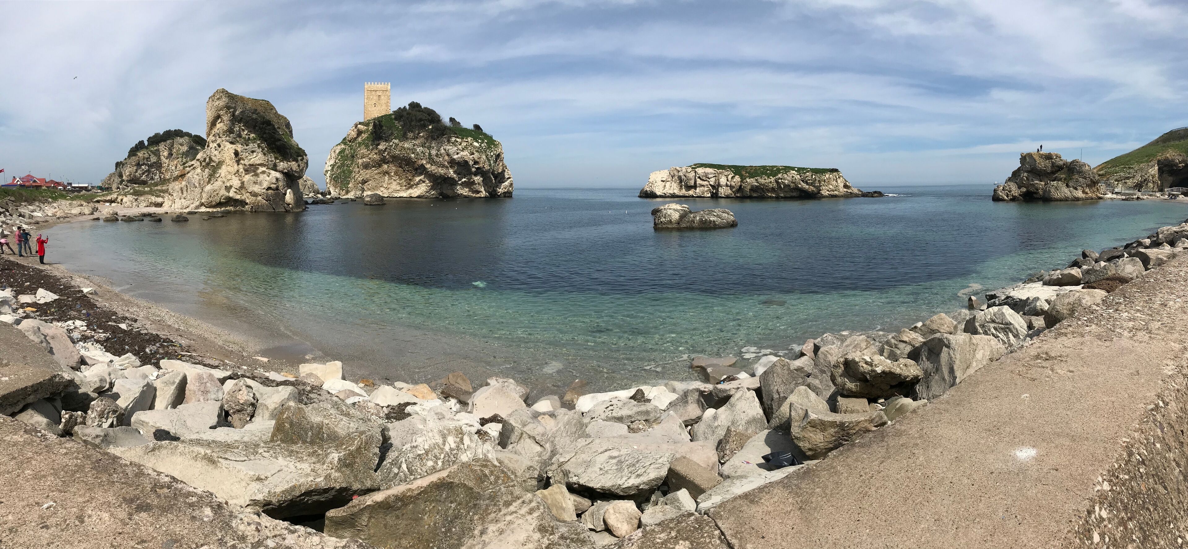 A coastal landscape with rocky formations, clear waters, and a tower on a prominent rock.