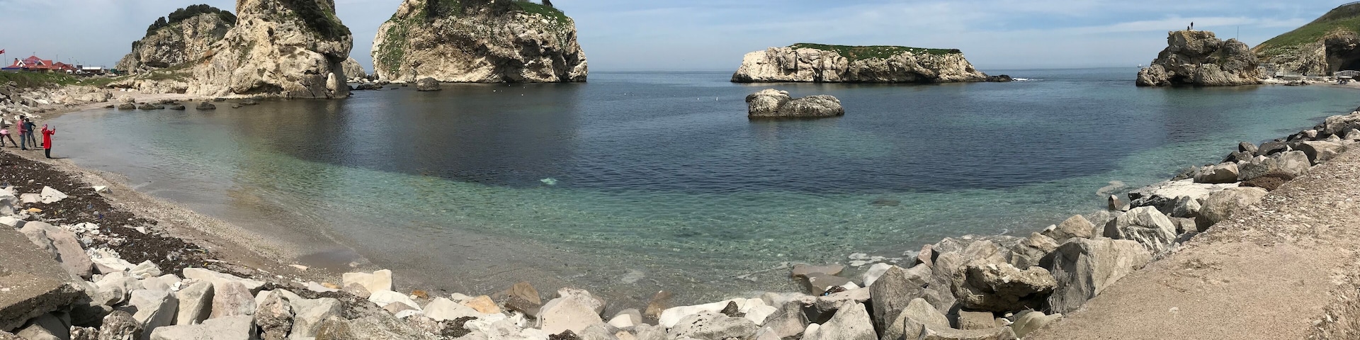 A coastal landscape with rocky formations, clear waters, and a tower on a prominent rock.