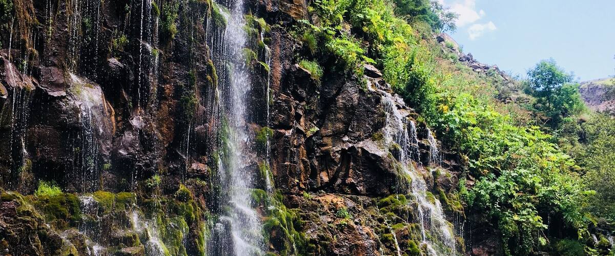 A waterfall cascading into a clear river surrounded by rocky terrain and lush greenery.