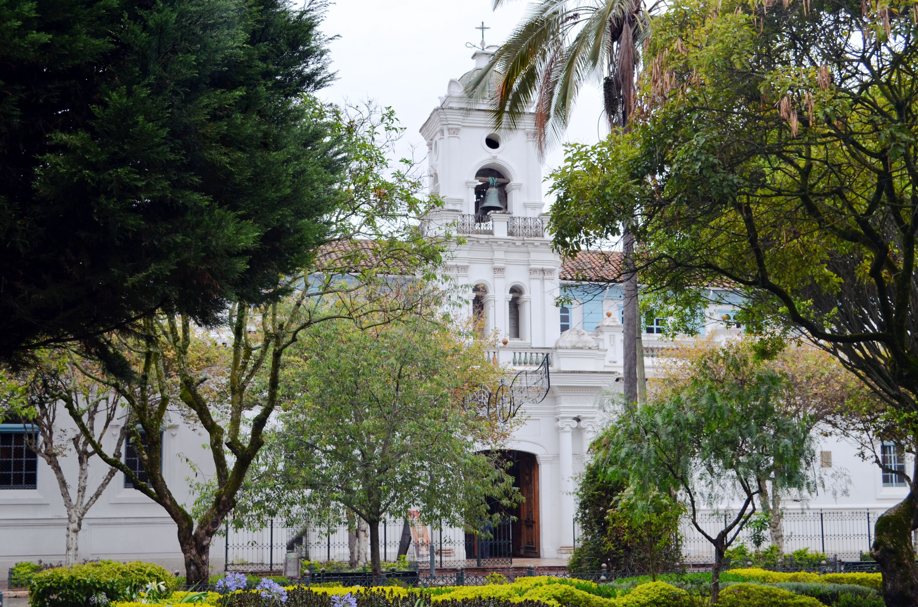 A white church with a bell tower surrounded by trees and well-maintained gardens.