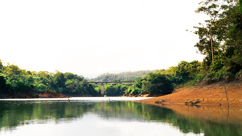A river with a bridge, surrounded by dense greenery and hills.