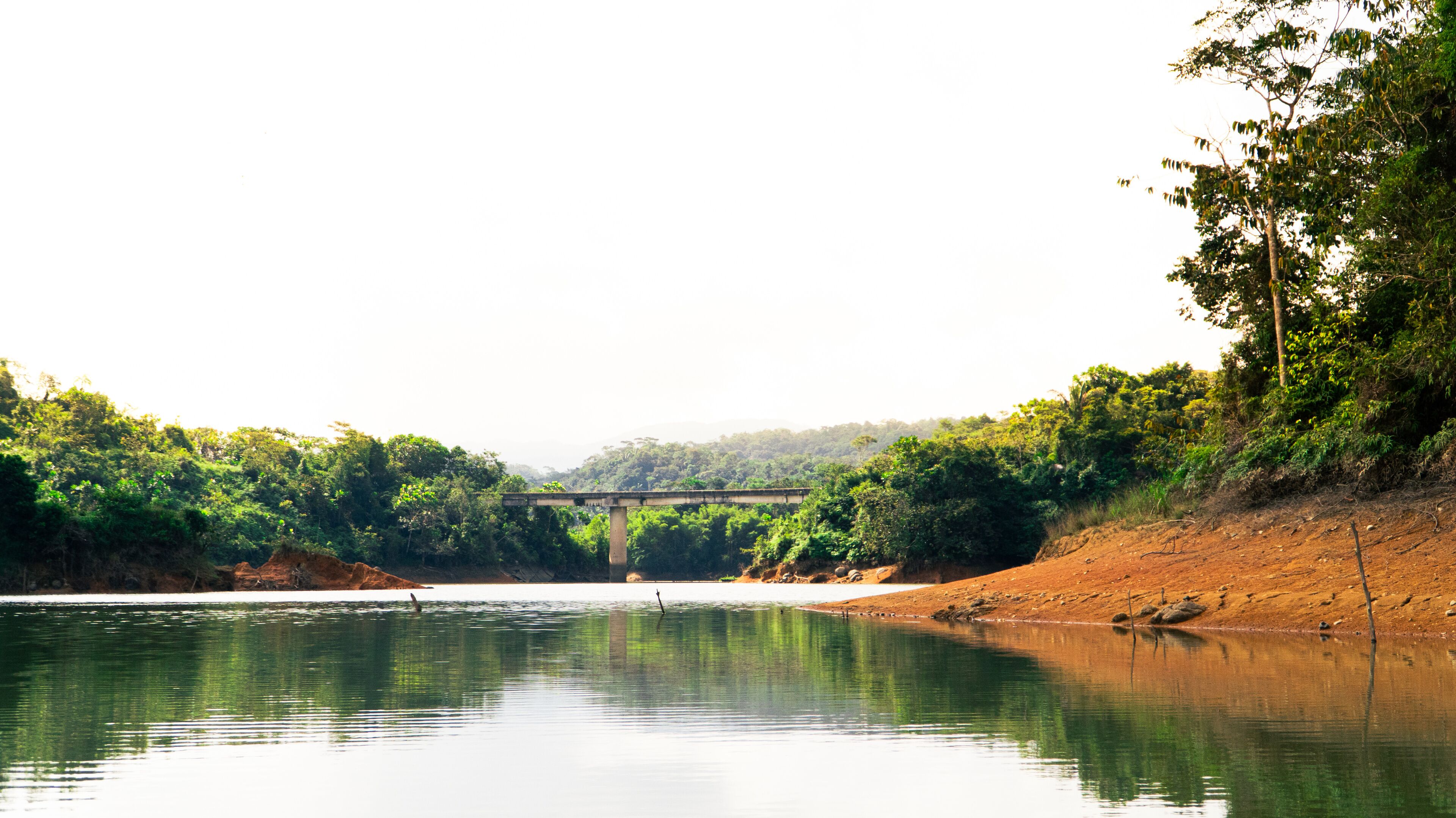 A river with a bridge, surrounded by dense greenery and hills.