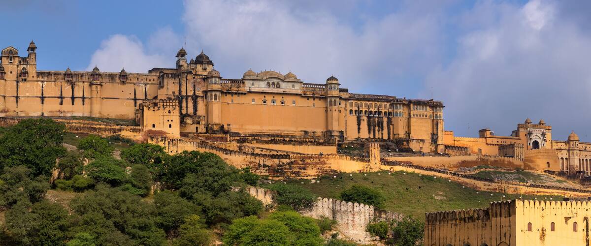 A historic fort with multiple towers and domes, surrounded by lush greenery and a clear sky.