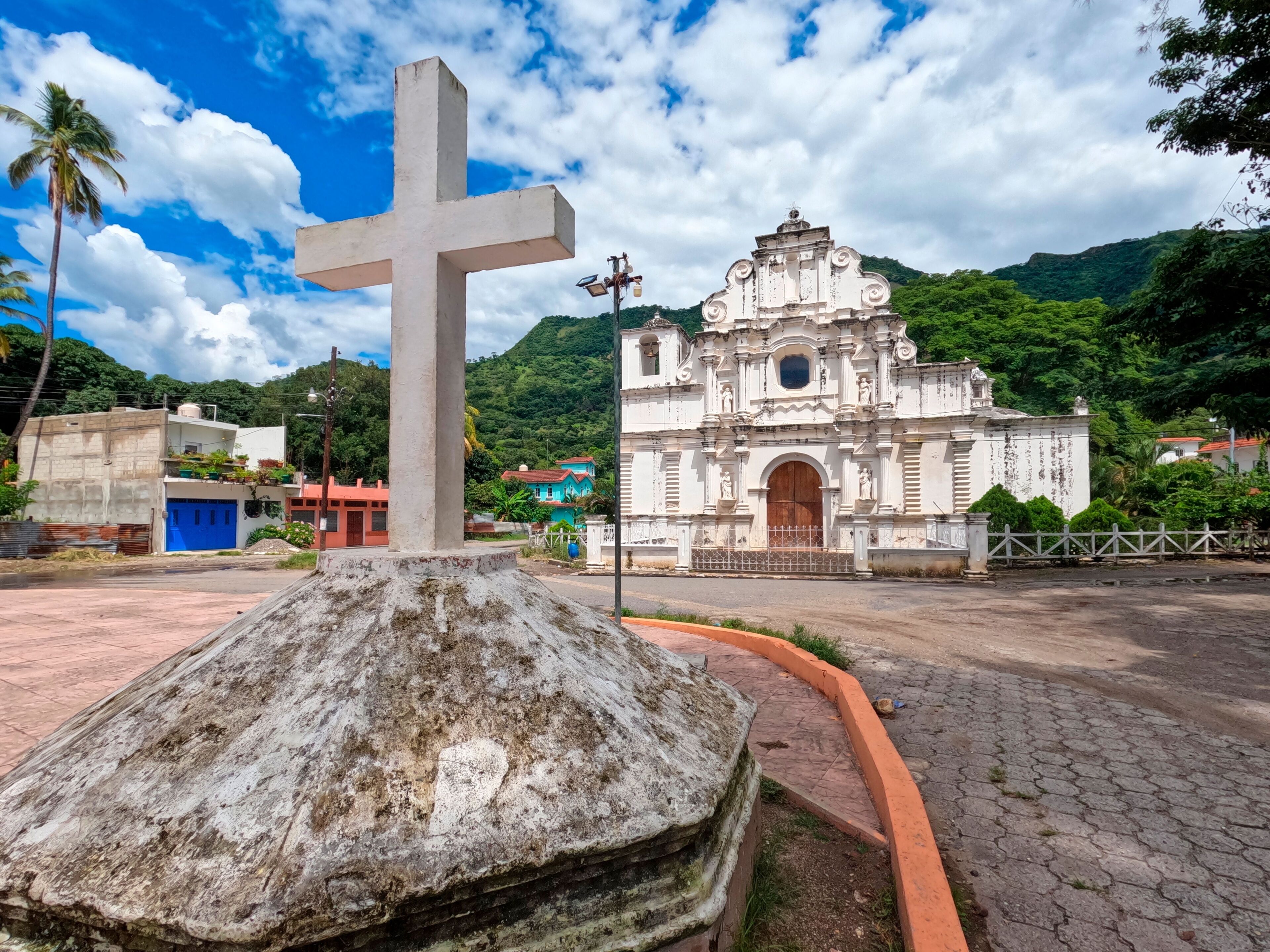 A large white cross, a historic church, and a mountainous landscape.